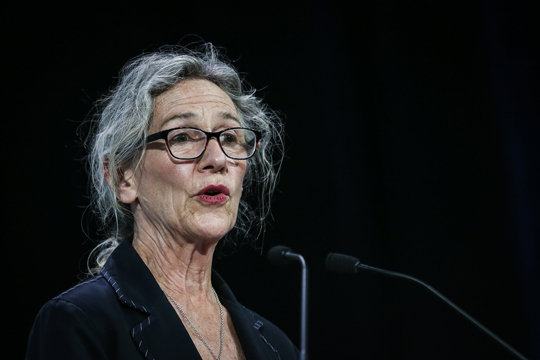 The Honorable Joyce Murray, Minister of Fisheries, Oceans and the Canadian Coast Guard. She wears a black blazer and glasses and is shown mid-speech behind the microphone.