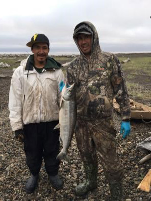 Photographie de Charlie Erigaktoak et de Danny Gordon Jr. tenant un saumon qu’ils ont pêché en 2016 à Shingle Point, au Yukon.