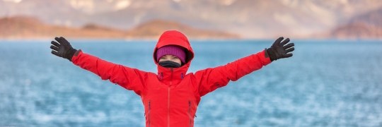 femme étendant ses bras devant un arrière-plan scénique avec un océan et des montagnes.