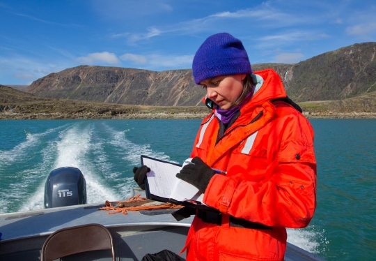 Femme scientifique prenant des notes dans un carnet de terrain sur un bateau.