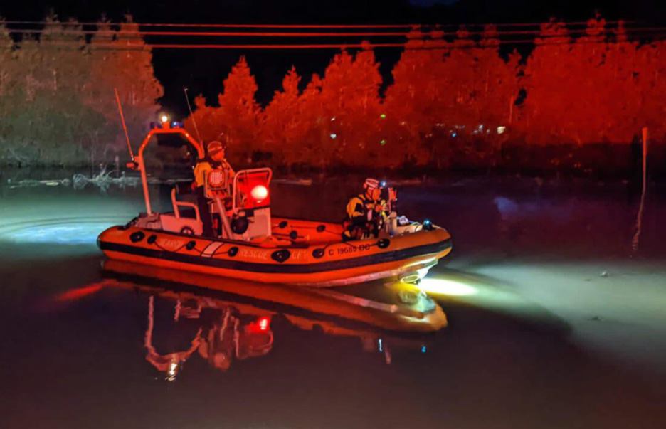 Photo de deux employés du MPO et de la Garde côtière. Ils sont équipés d'un équipement d'urgence à bord d'un zodiac, patrouillant la nuit sur un fleuve Fraser inondé.