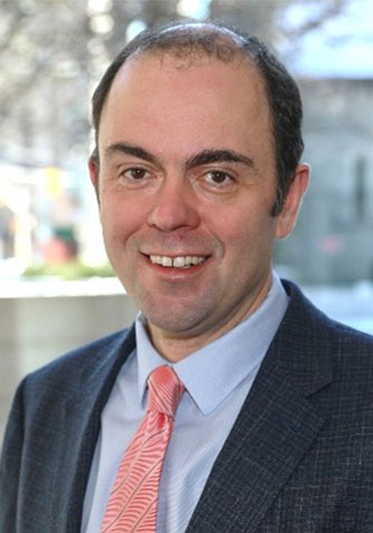 Portrait d'Adam Burns, sous-ministre adjoint à la Gestion des pêches et des ports, et cochampion de l'accessibilité; un homme blanc aux cheveux courts et foncés portant une chemise bleu pâle, une cravate rose et une veste bleu marine.