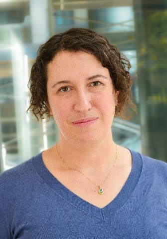Portrait de Darcy Demarsico, directrice générale - pêches et politique internationale, et co-championne de l'accessibilité; une femme blanche aux cheveux foncés, mi-longs et bouclés, portant un chandail bleu.