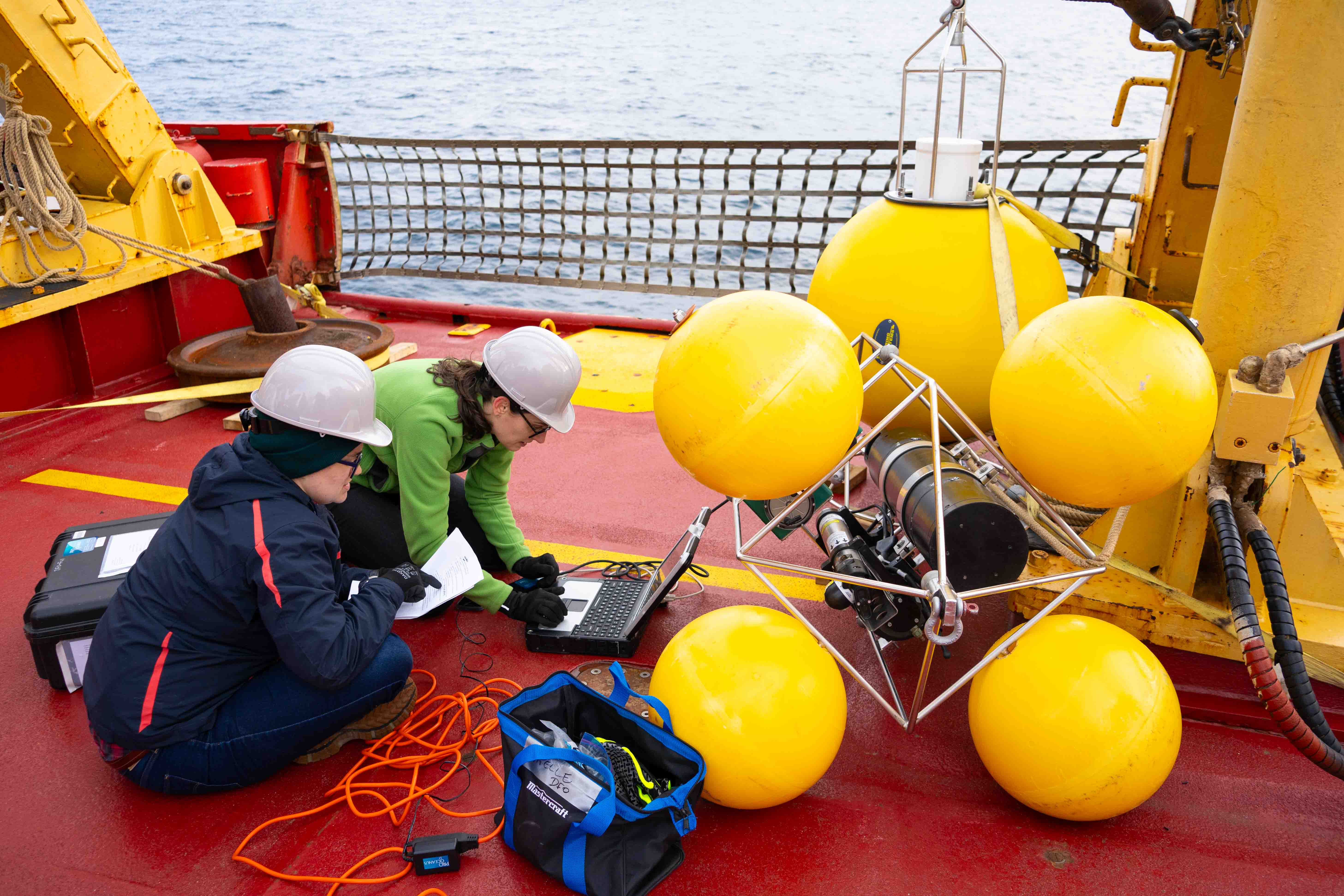 DFO scientists Elizabeth Kitching and Tonya Burgers (from left to right) programming mooring sensors prior to deployment during the 2024 ArcticCORE marine survey onboard CCGS Amundsen. Photo credit: Fatma Dhifallah.