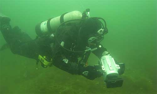 This diver is using an underwater video camera to film the area marked by transect lines (which mark an area 100 m x 2 m) before they start to dig for lobsters to record their length and sex. Photo credit: Fisheries and Oceans Canada (DFO).